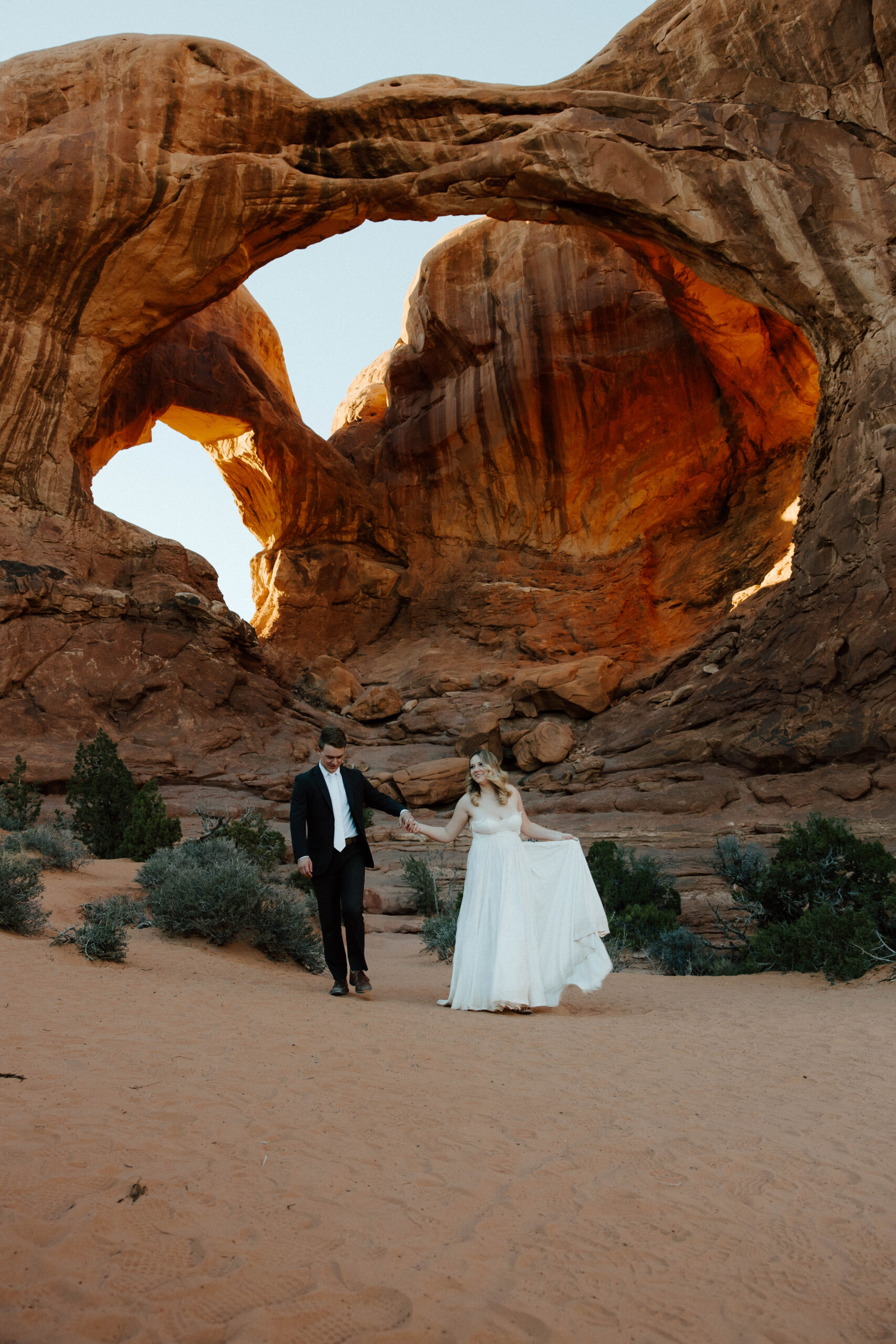 Moab elopement photographer capturing couple walking under natural arch formation in Arches National Park