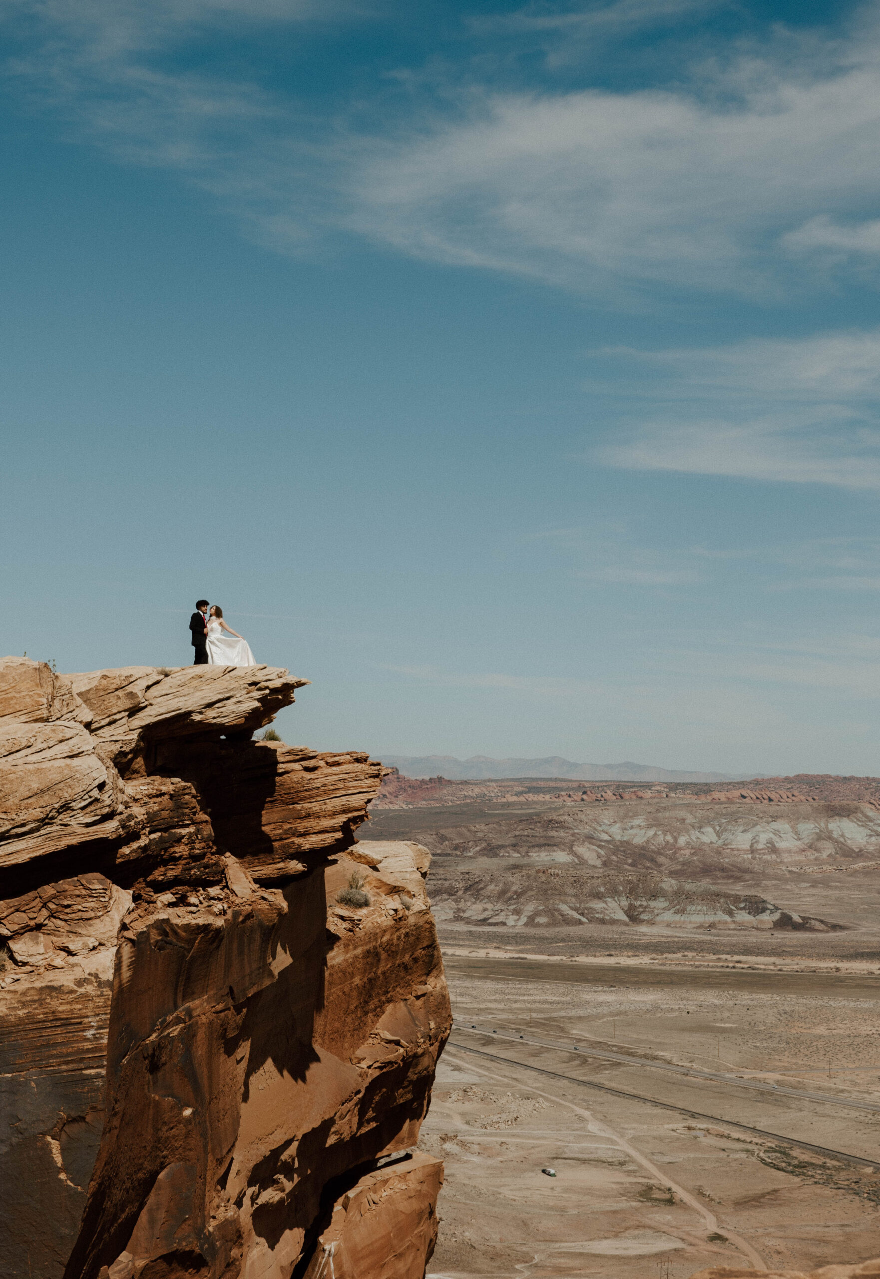 Moab elopement photographer capturing couple on dramatic rock cliff with panoramic desert views.