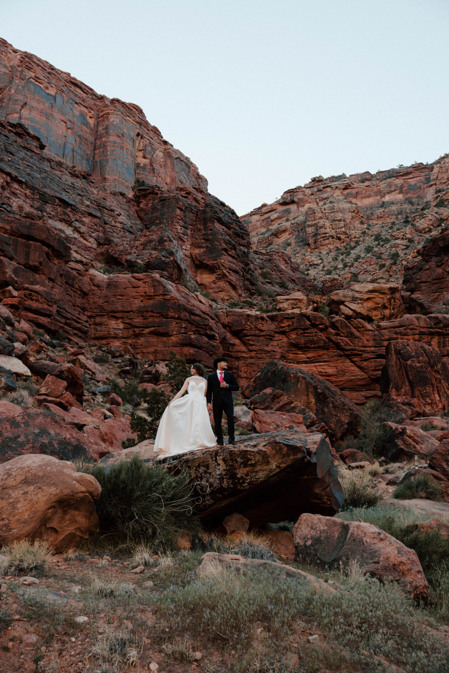 Couple standing in Moab Utah surrounded by red rocks. Holding hands standing on a red rock.